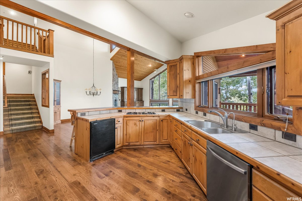 Kitchen featuring backsplash, brown cabinets, light countertops, a healthy amount of sunlight, light hardwood floors, lofted ceiling with beams, and stainless steel appliances