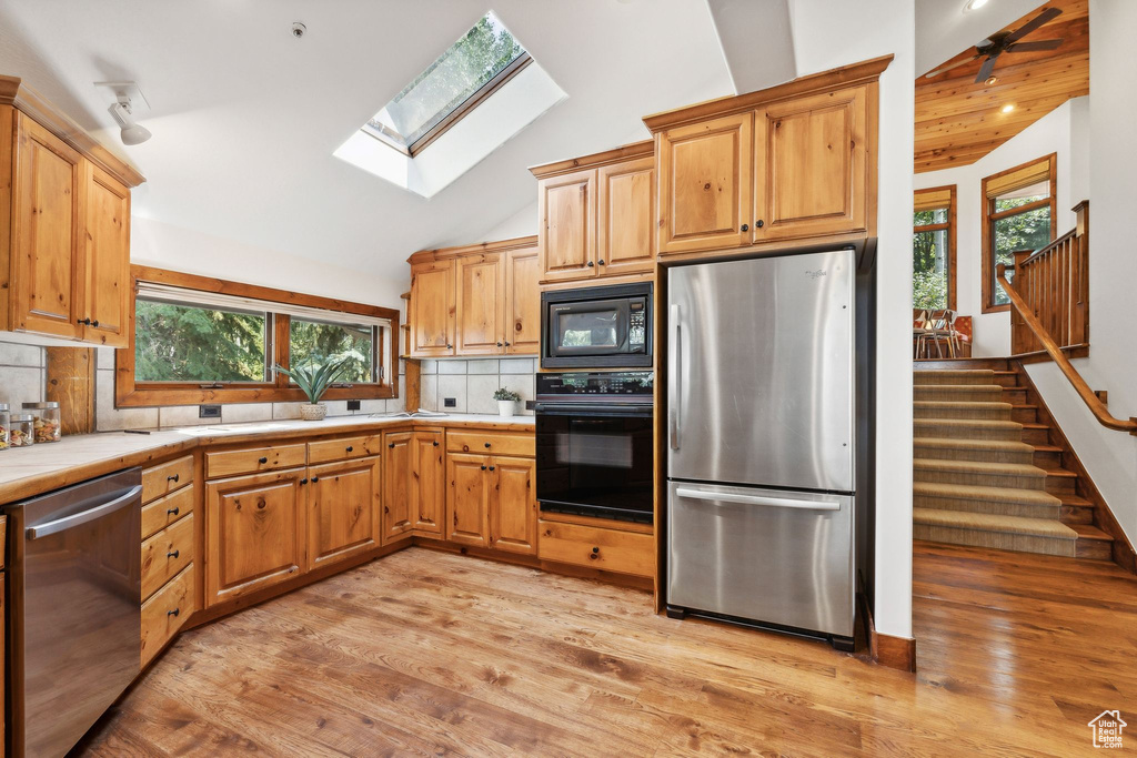 Kitchen with tasteful backsplash, black appliances, light wood-type flooring, tile countertops, and a skylight