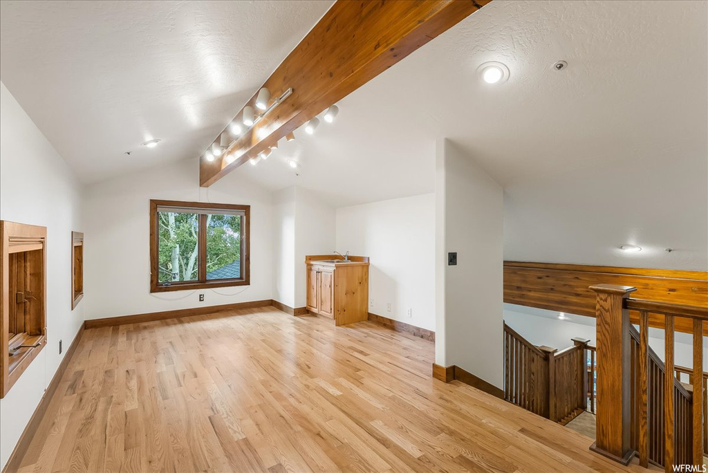 Additional living space featuring lofted ceiling with beams and light hardwood floors