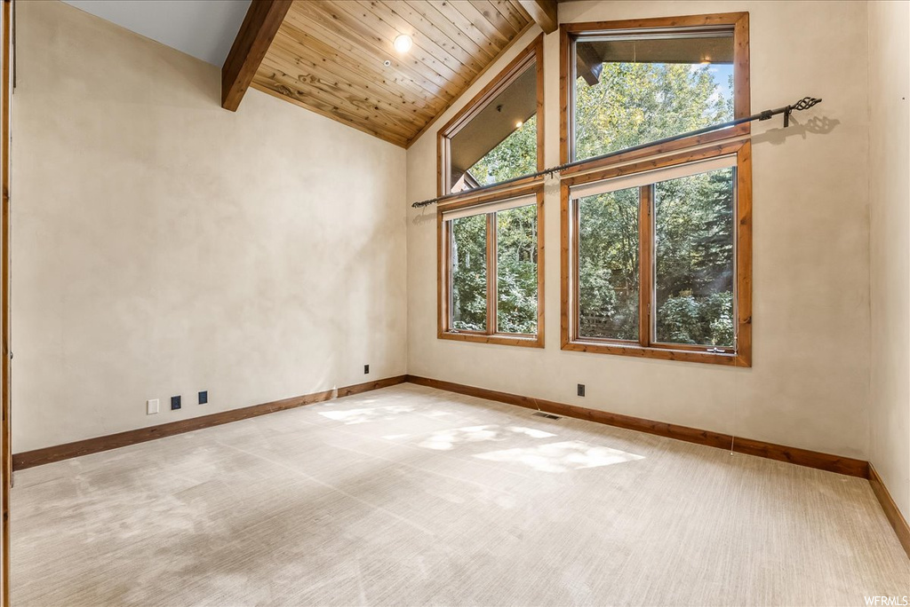 Unfurnished room featuring a healthy amount of sunlight, light carpet, wooden ceiling, lofted ceiling with beams, and a high ceiling