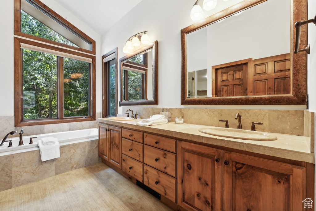 Bathroom with decorative backsplash, double vanity, tiled tub, and lofted ceiling