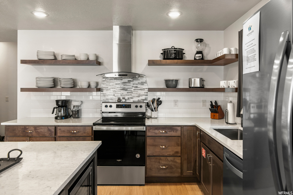 Kitchen featuring backsplash, dark brown cabinets, light countertops, appliances with stainless steel finishes, hardwood floors, and ventilation hood