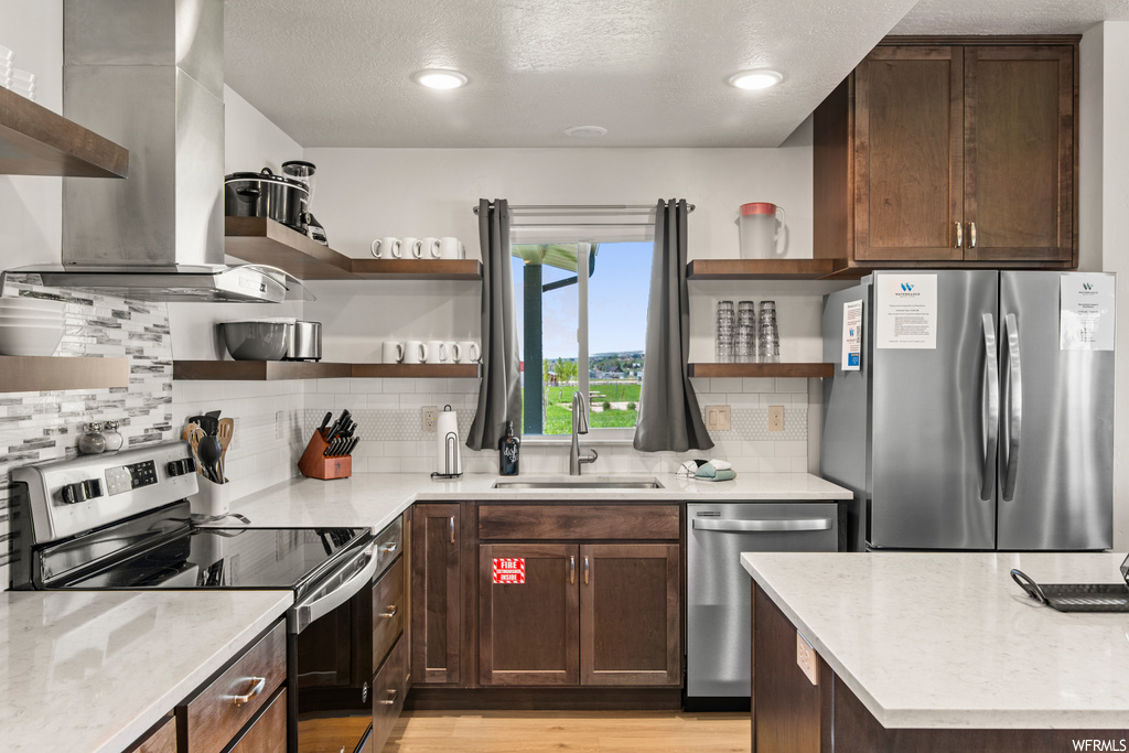 Kitchen featuring a textured ceiling, backsplash, light countertops, appliances with stainless steel finishes, dark brown cabinetry, hardwood floors, and extractor fan