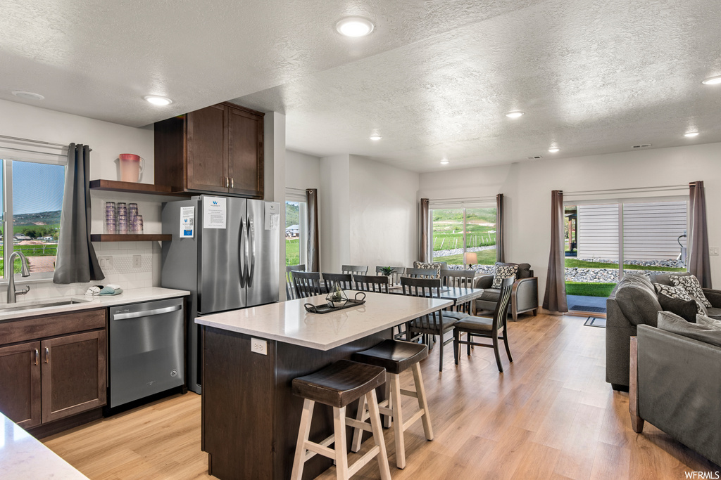 Kitchen with stainless steel dishwasher, a textured ceiling, a center island, light countertops, dark brown cabinets, and light hardwood floors