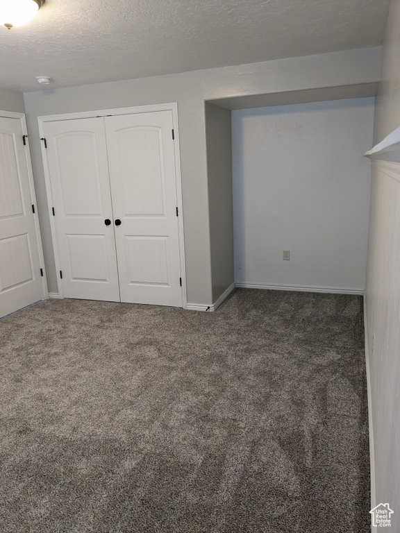 Unfurnished bedroom featuring a textured ceiling and dark carpet