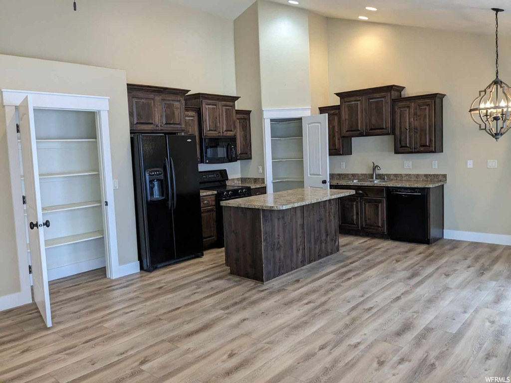 Kitchen with black appliances, an inviting chandelier, pendant lighting, light hardwood / wood-style flooring, and a center island