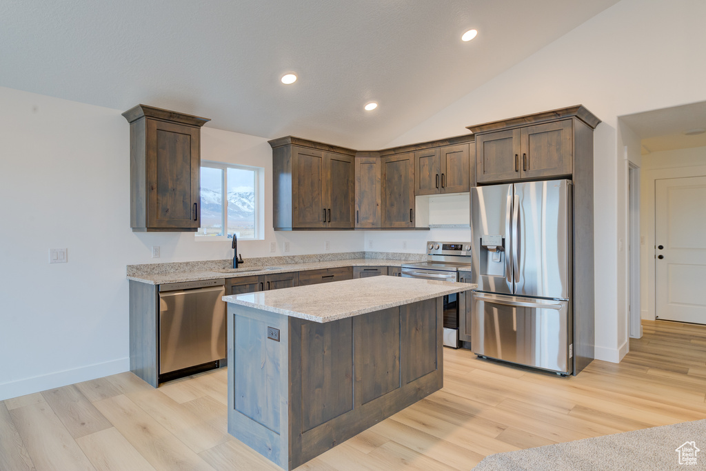 Kitchen featuring a kitchen island, light stone counters, vaulted ceiling, appliances with stainless steel finishes, and light hardwood / wood-style flooring