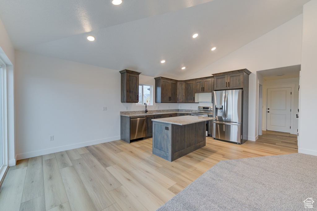 Kitchen with a kitchen island, light wood-type flooring, light stone counters, dark brown cabinets, and appliances with stainless steel finishes