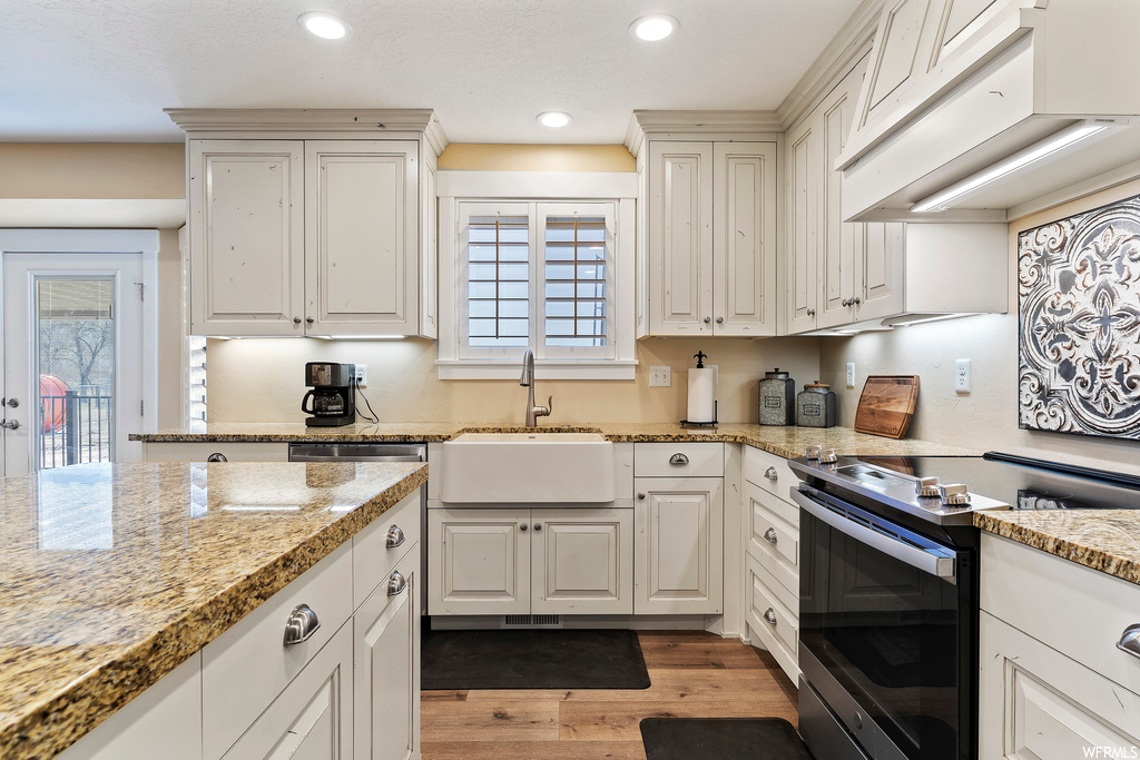 Kitchen featuring plenty of natural light, white cabinetry, custom range hood, hardwood floors, and electric range