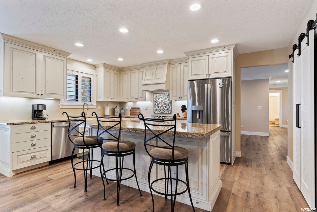 Kitchen featuring a textured ceiling, white cabinets, a kitchen island, light hardwood flooring, premium range hood, and stainless steel appliances