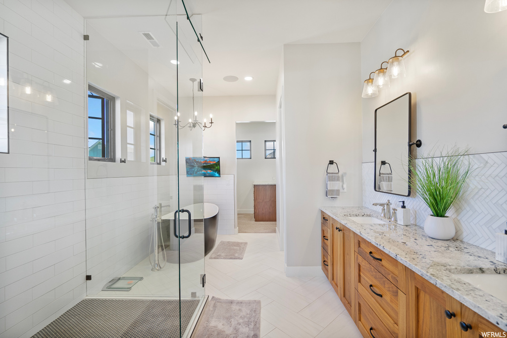 Bathroom featuring an enclosed shower, dual bowl vanity, mirror, tile walls, and light tile floors