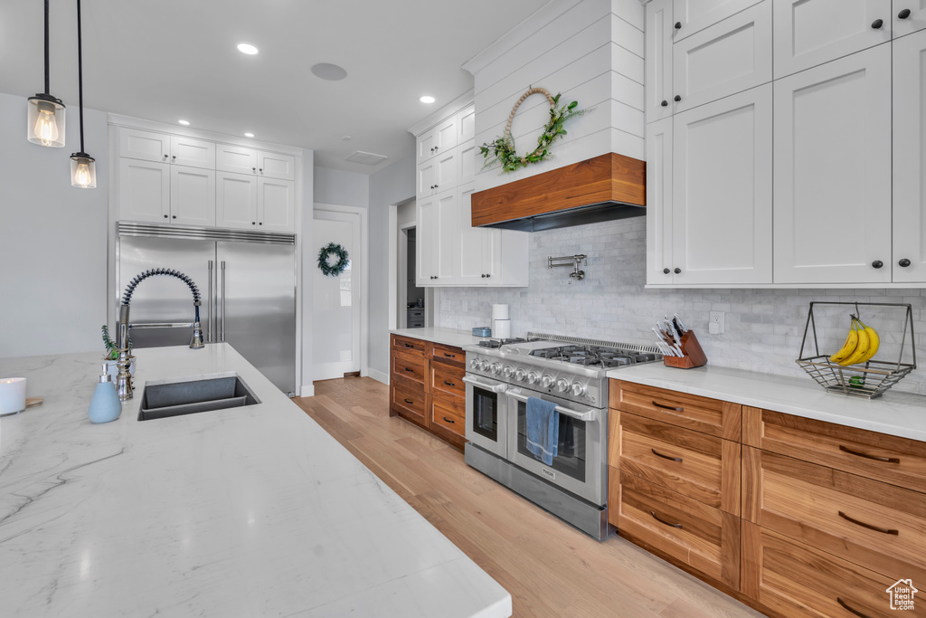 Kitchen featuring high quality appliances, pendant lighting, tasteful backsplash, white cabinetry, and light wood-type flooring