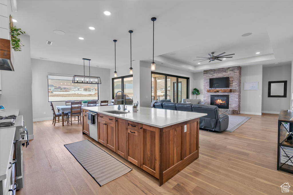 Kitchen with hanging light fixtures, ceiling fan with notable chandelier, a kitchen island with sink, light hardwood / wood-style floors, and a brick fireplace