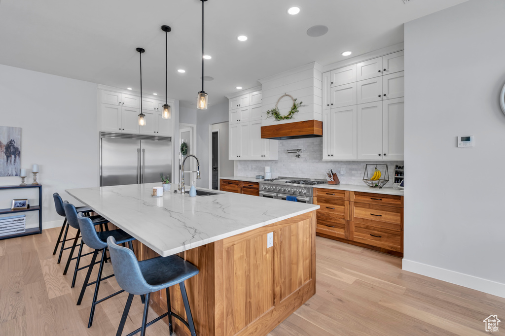 Kitchen featuring high quality appliances, light wood-type flooring, white cabinetry, and a center island with sink