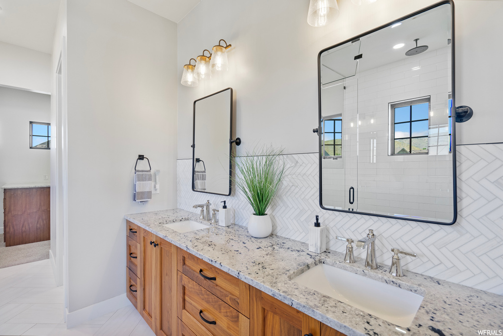 Bathroom featuring double sink vanity, a shower with door, mirror, backsplash, and light tile floors