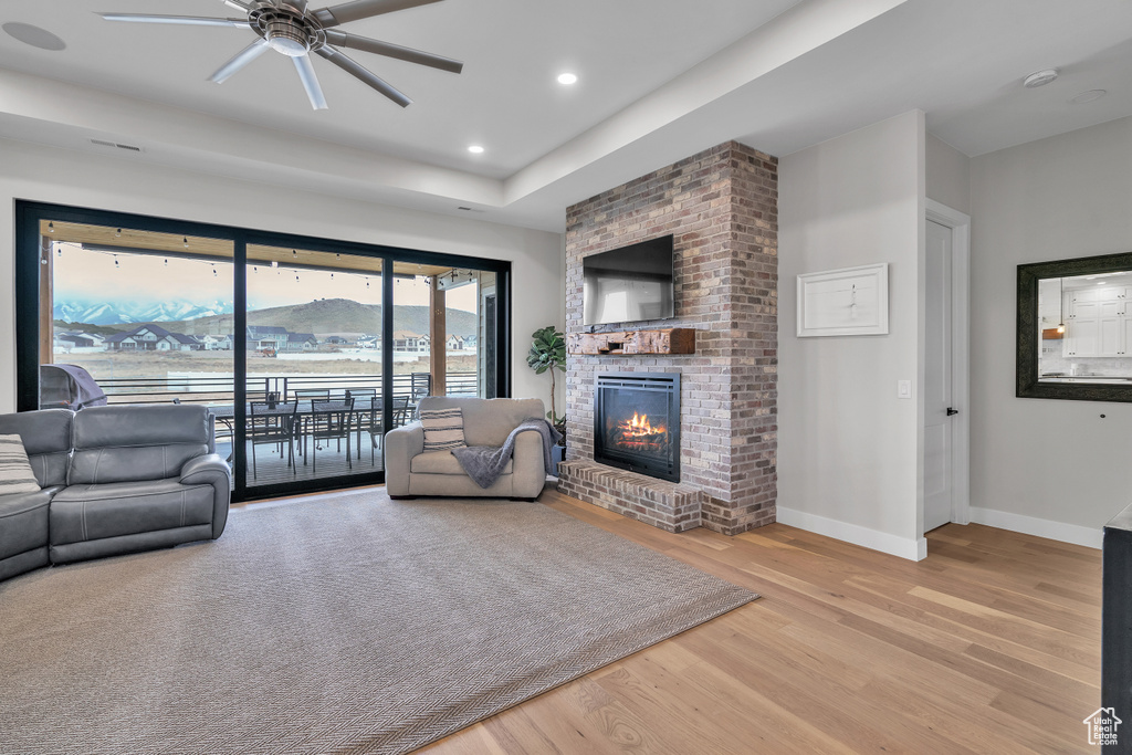 Living room with ceiling fan, brick wall, a fireplace, and light hardwood / wood-style floors