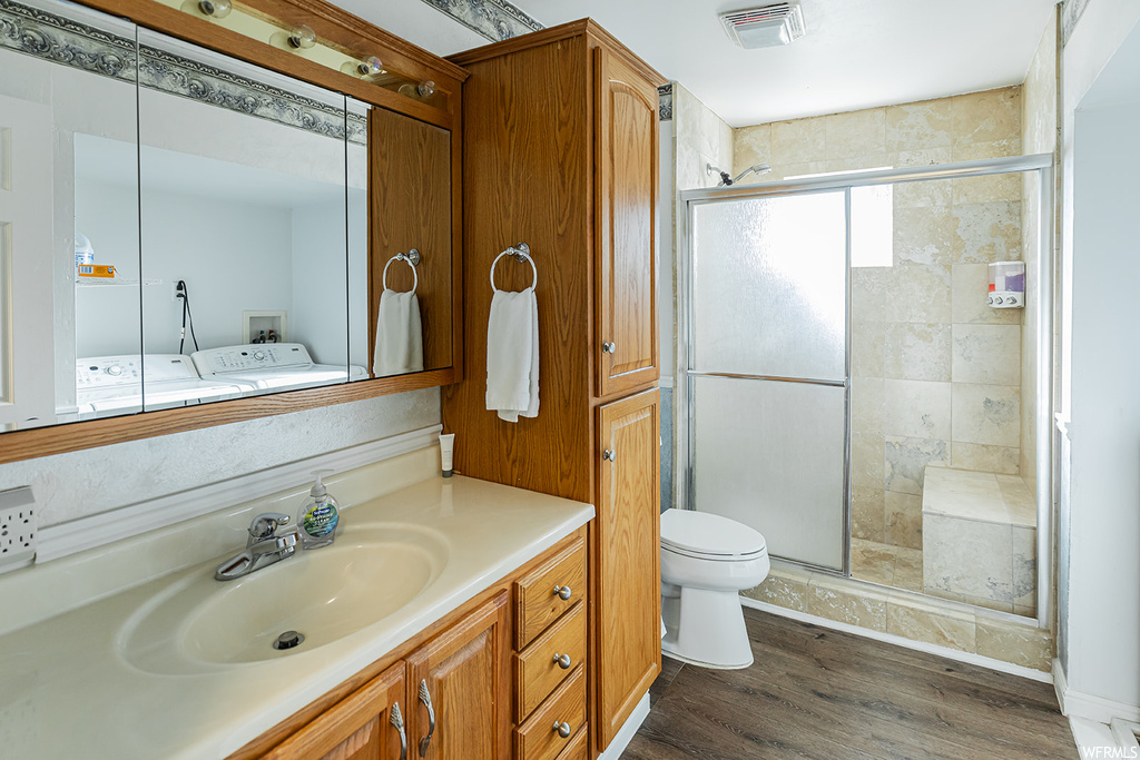 Bathroom with washing machine and clothes dryer, mirror, a shower with door, light hardwood floors, and vanity