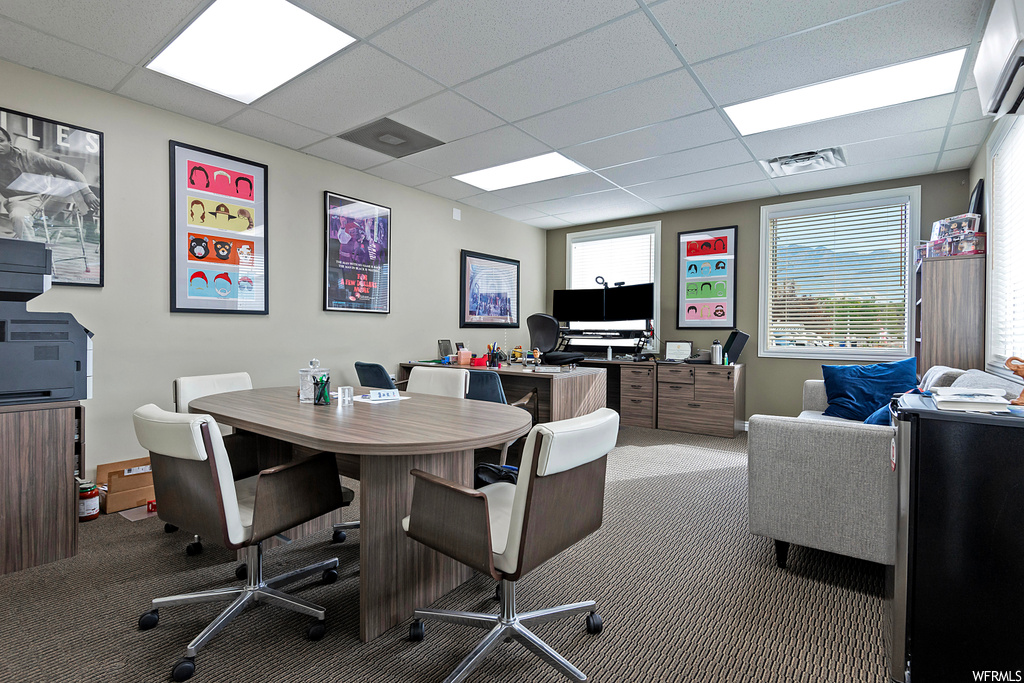Carpeted office with a drop ceiling, plenty of natural light, and a wall mounted air conditioner