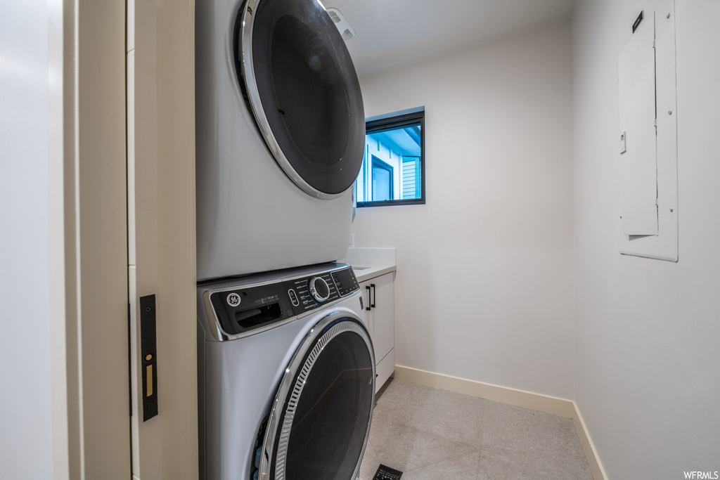 Laundry room with stacked washing maching and dryer and light tile floors
