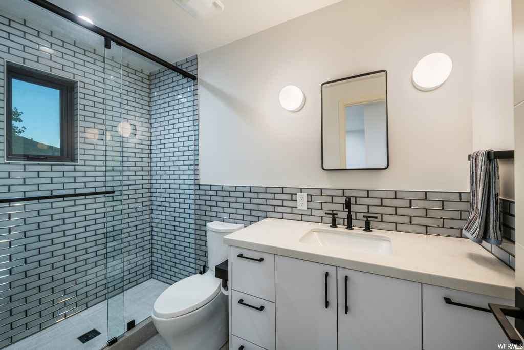 Bathroom with oversized vanity, mirror, a shower with shower door, tile walls, and backsplash