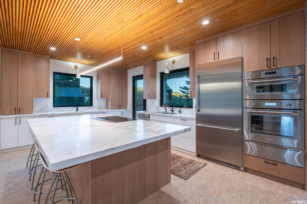 Kitchen with light stone counters, backsplash, a kitchen island, and stainless steel appliances