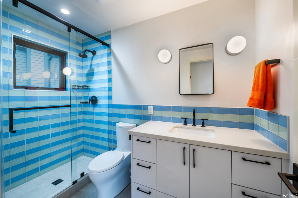 Bathroom with vanity, mirror, a shower with shower door, tile walls, and backsplash