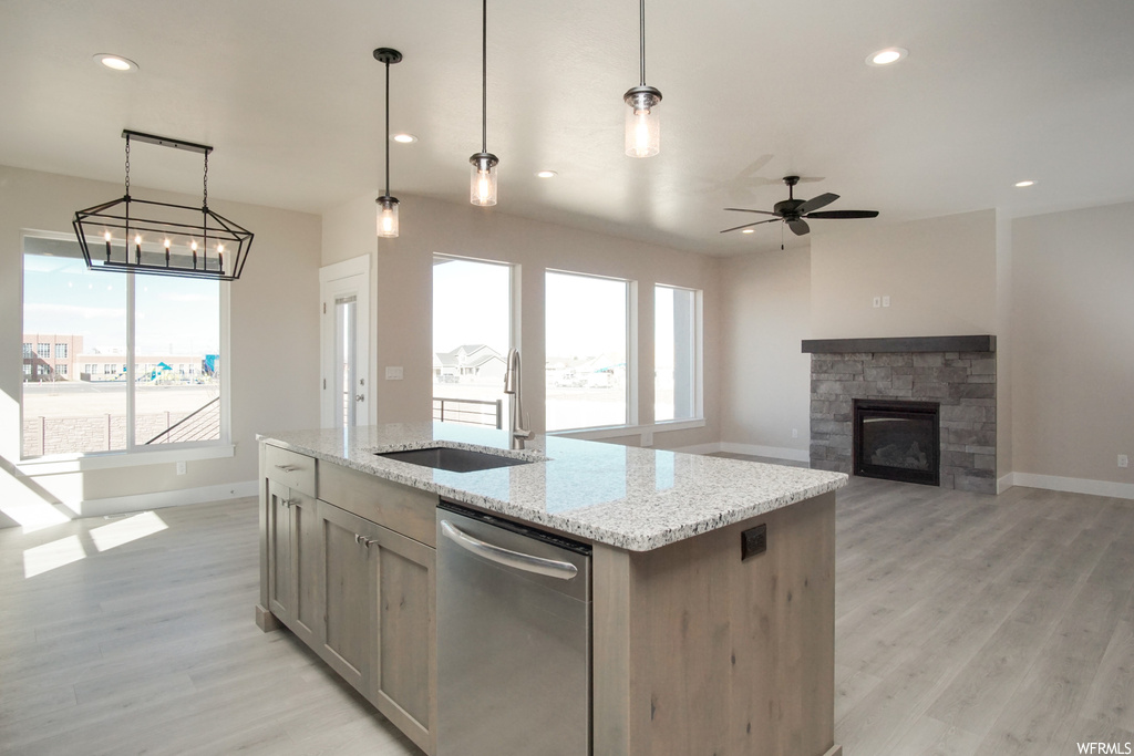 Kitchen with stainless steel dishwasher, decorative light fixtures, a fireplace, light stone countertops, light hardwood floors, and ceiling fan