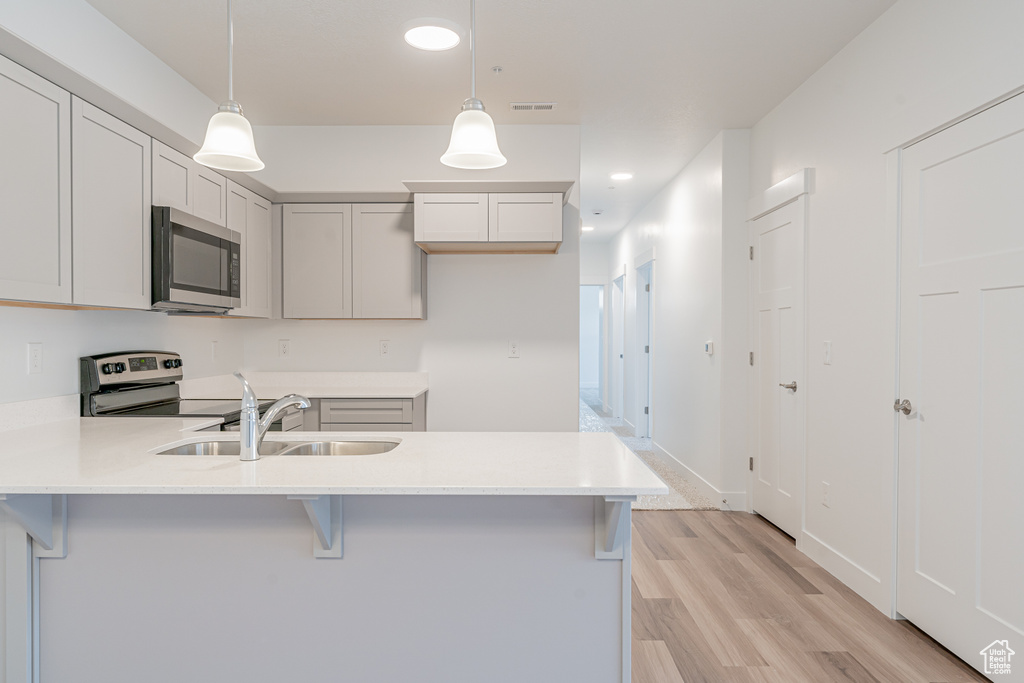 Kitchen featuring kitchen peninsula, decorative light fixtures, stainless steel appliances, light hardwood / wood-style floors, and sink