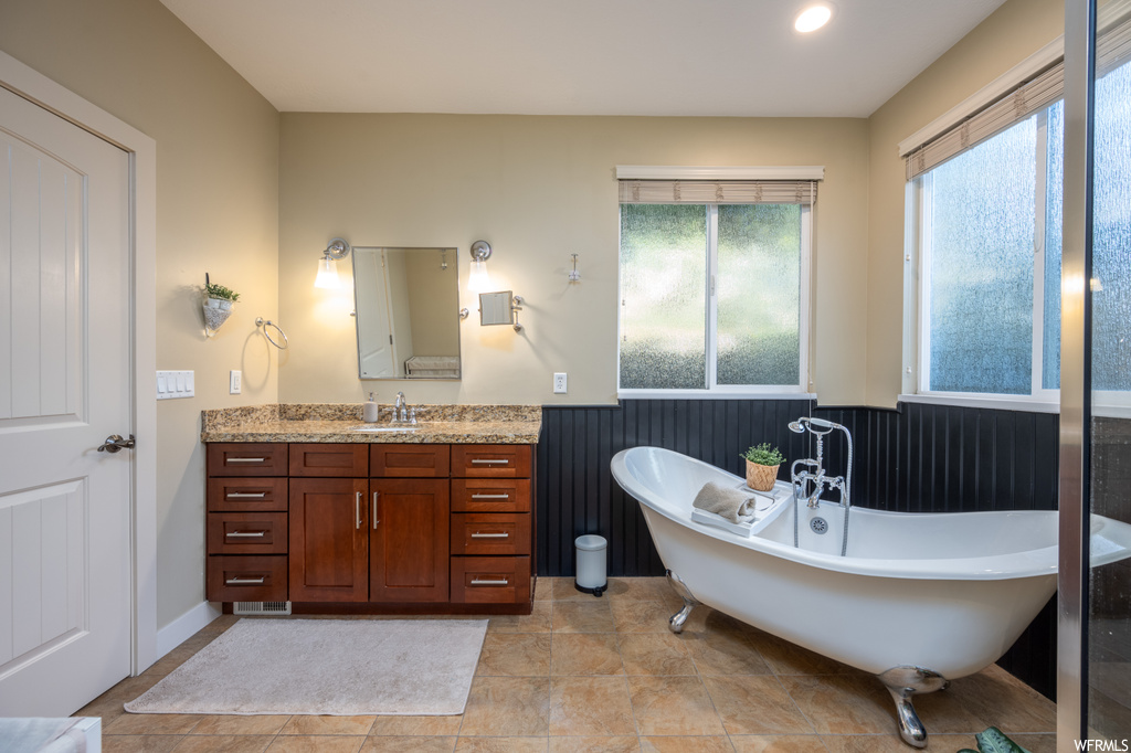 Bathroom with light tile flooring, a bathing tub, mirror, and vanity