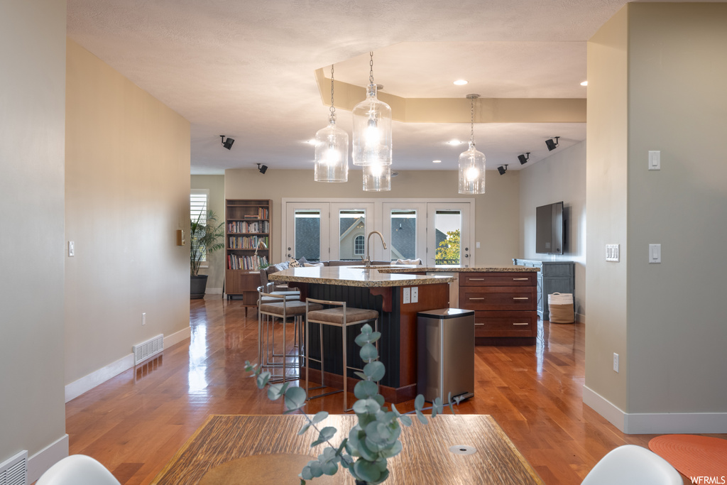 Kitchen featuring pendant lighting, light hardwood floors, and kitchen island with sink