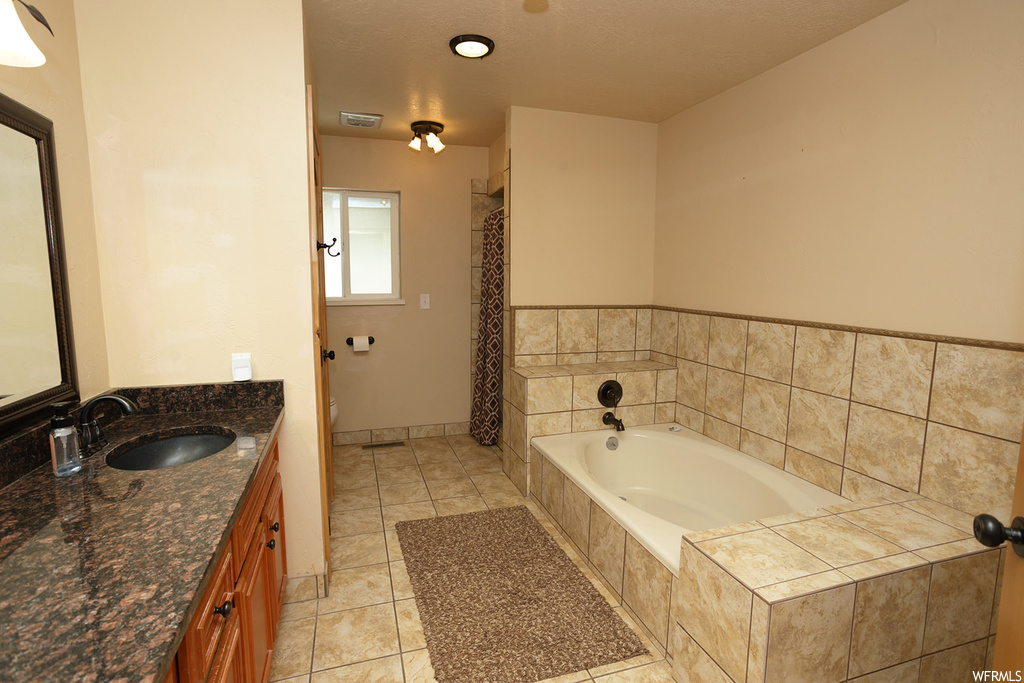 Bathroom with tiled tub, tile floors, and vanity
