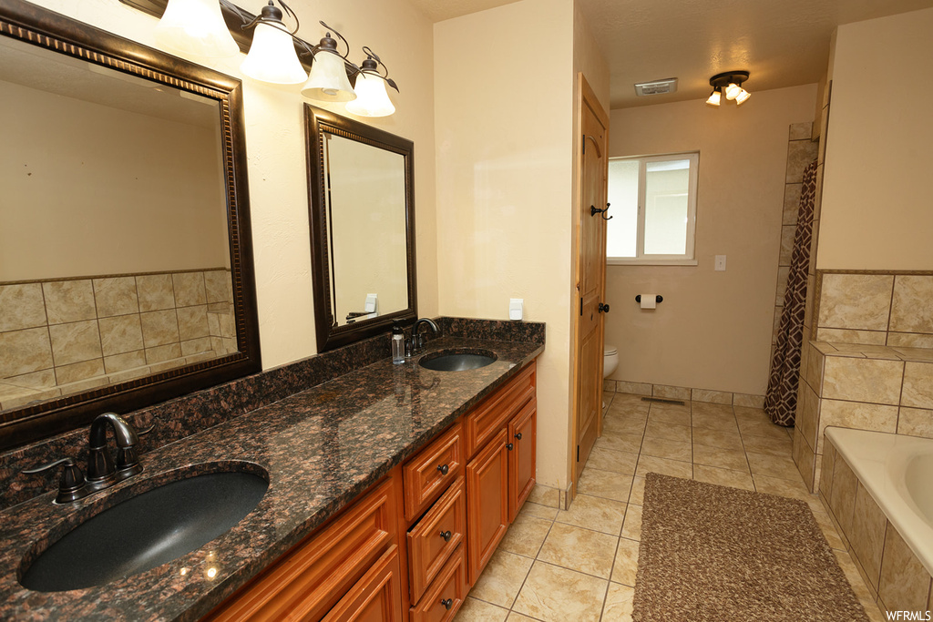 Bathroom with dual bowl vanity, tile floors, a relaxing tiled bath, and toilet