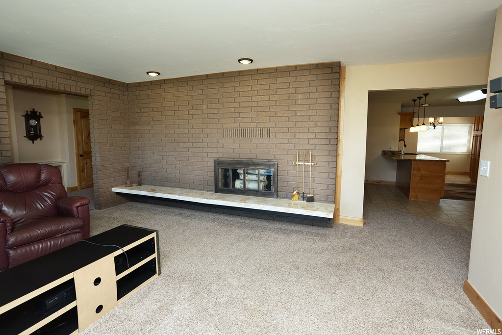 Unfurnished living room featuring a notable chandelier, light colored carpet, a fireplace, and brick wall