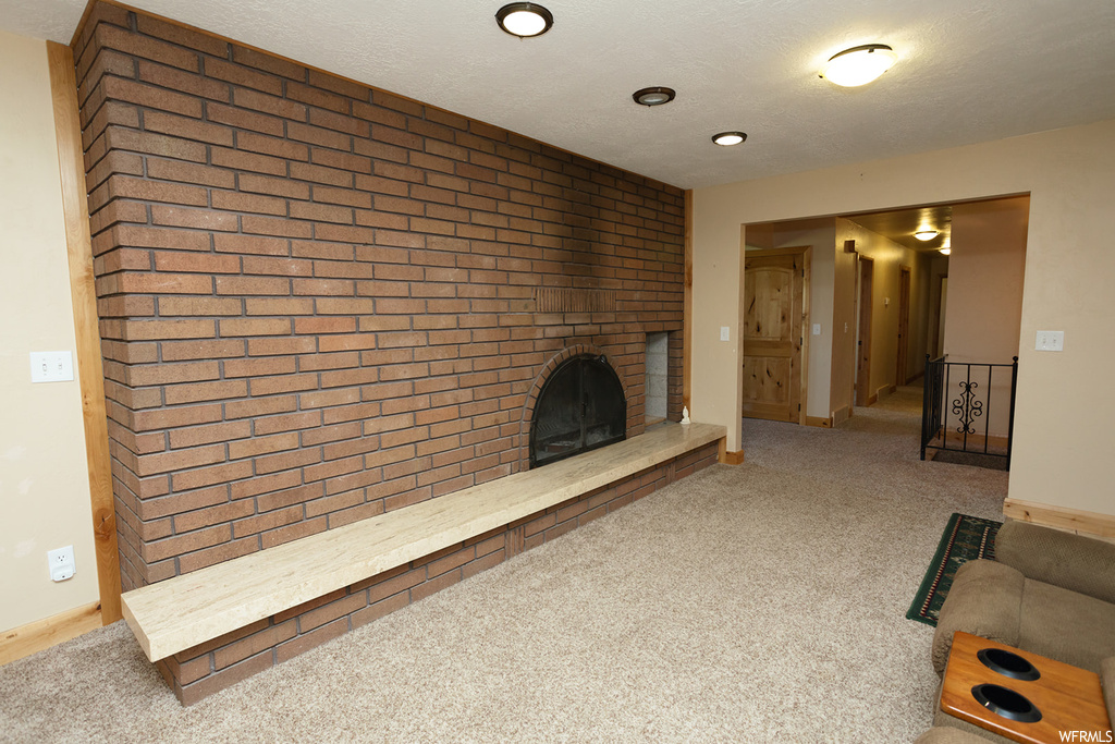 Unfurnished living room featuring a textured ceiling, brick wall, carpet, and a fireplace