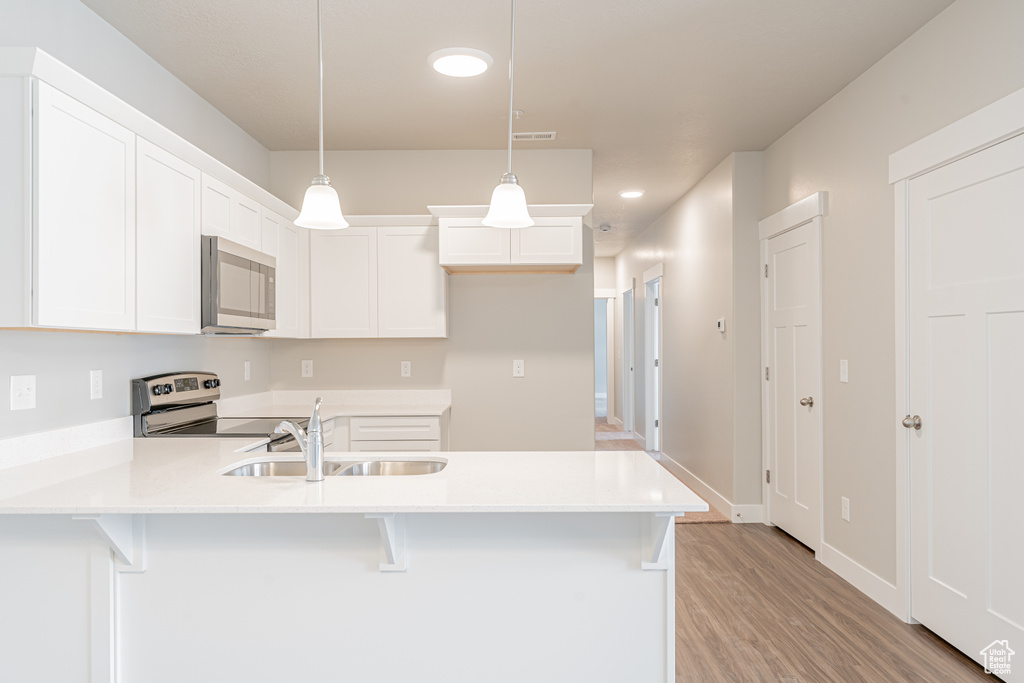 Kitchen with range with electric stovetop, white cabinets, sink, pendant lighting, and light wood-type flooring