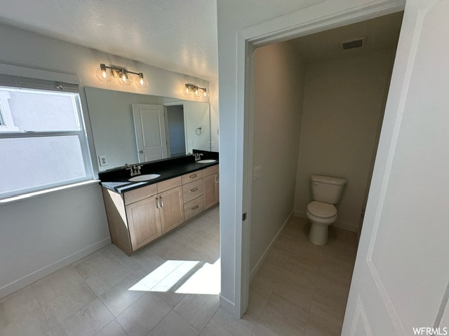 Bathroom with double large vanity, mirror, and light tile floors