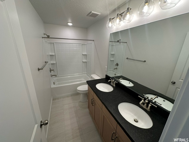 Full bathroom with a textured ceiling, mirror, light tile floors,  shower combination, and double large vanity