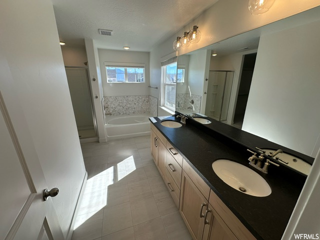 Bathroom with double sink vanity, a textured ceiling, mirror, separate shower and tub enclosures, and light tile floors