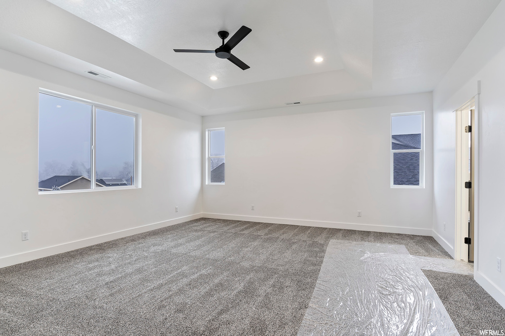 Carpeted empty room with a tray ceiling and ceiling fan