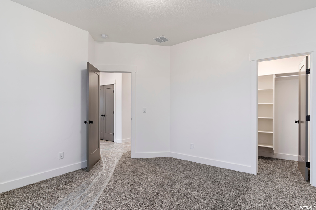 Unfurnished bedroom with a walk in closet and light colored carpet