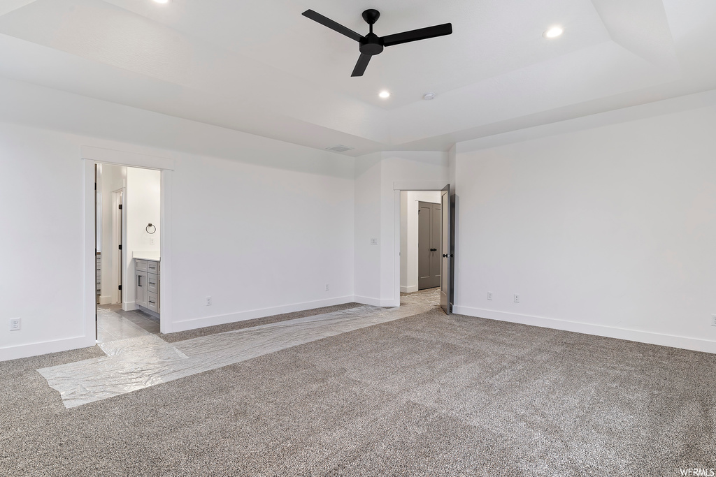 Empty room featuring ceiling fan, a tray ceiling, and light carpet