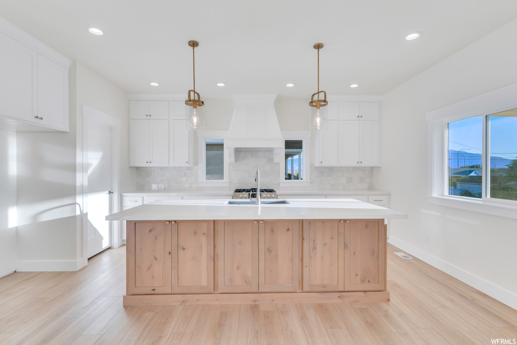 Kitchen featuring decorative light fixtures, backsplash, light countertops, white cabinetry, and light hardwood flooring