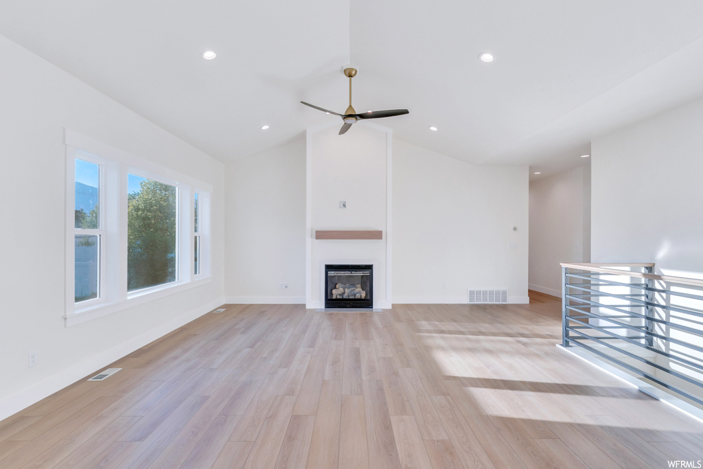 Living room featuring light hardwood floors, ceiling fan, lofted ceiling, a fireplace, and a high ceiling