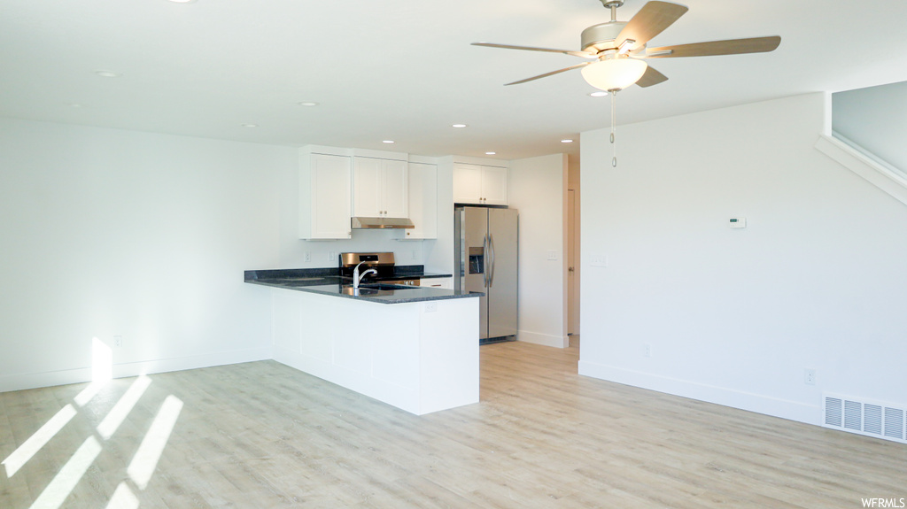 Kitchen featuring ceiling fan, stainless steel fridge, white cabinets, light hardwood flooring, and countertops dark