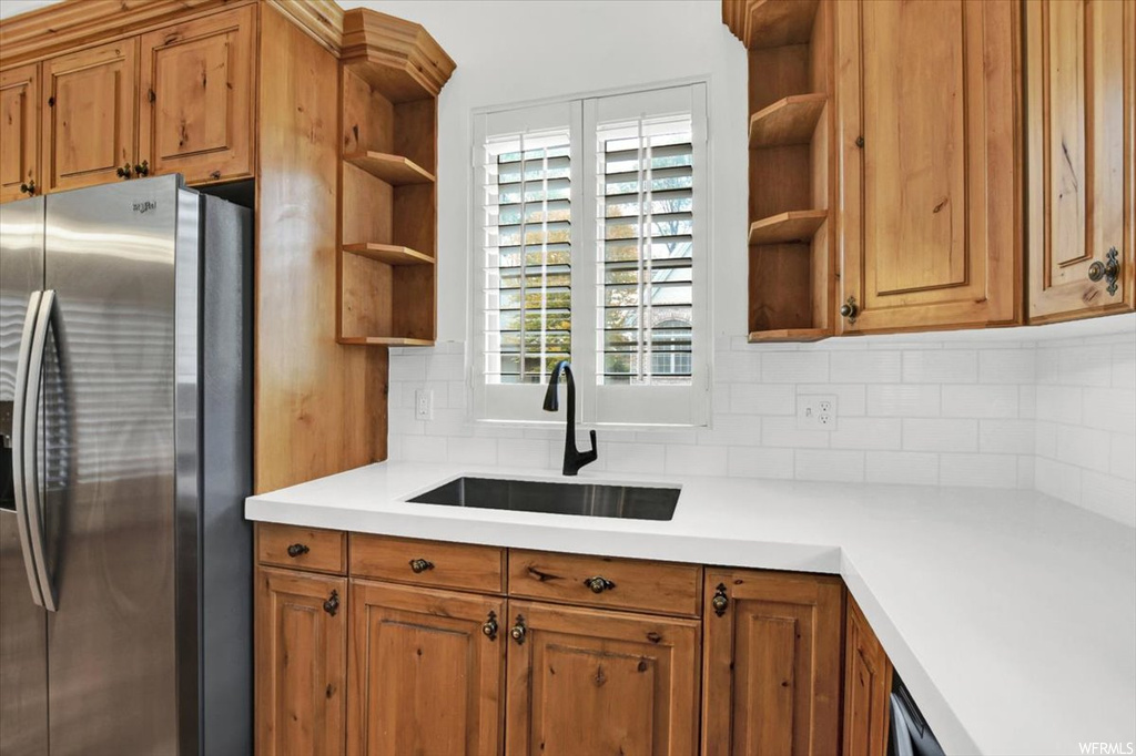 Kitchen with sink, plenty of natural light, tasteful backsplash, and stainless steel refrigerator with ice dispenser