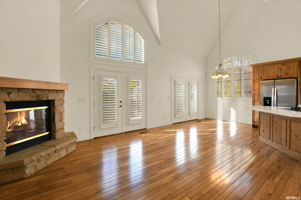 Unfurnished living room featuring a fireplace, a wealth of natural light, a high ceiling, and light hardwood / wood-style flooring