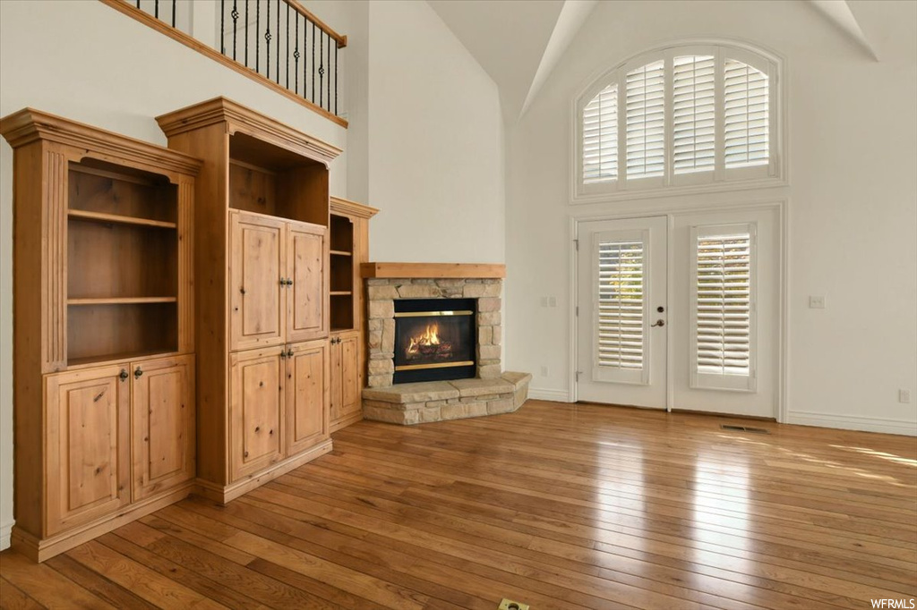 Unfurnished living room featuring a fireplace, a towering ceiling, light hardwood / wood-style floors, and french doors
