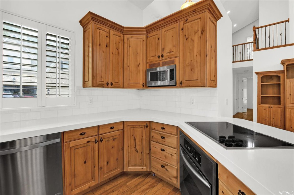 Kitchen with light hardwood / wood-style floors, backsplash, lofted ceiling, and black appliances