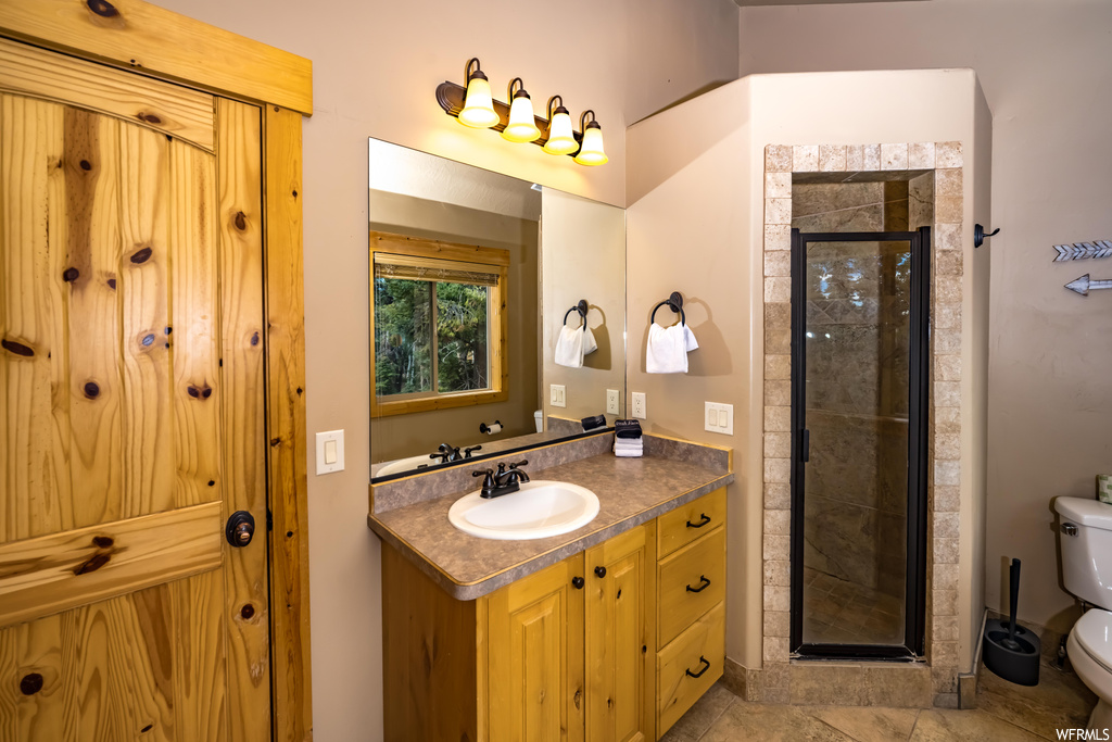 Bathroom featuring light tile floors, a shower with shower door, mirror, and vanity