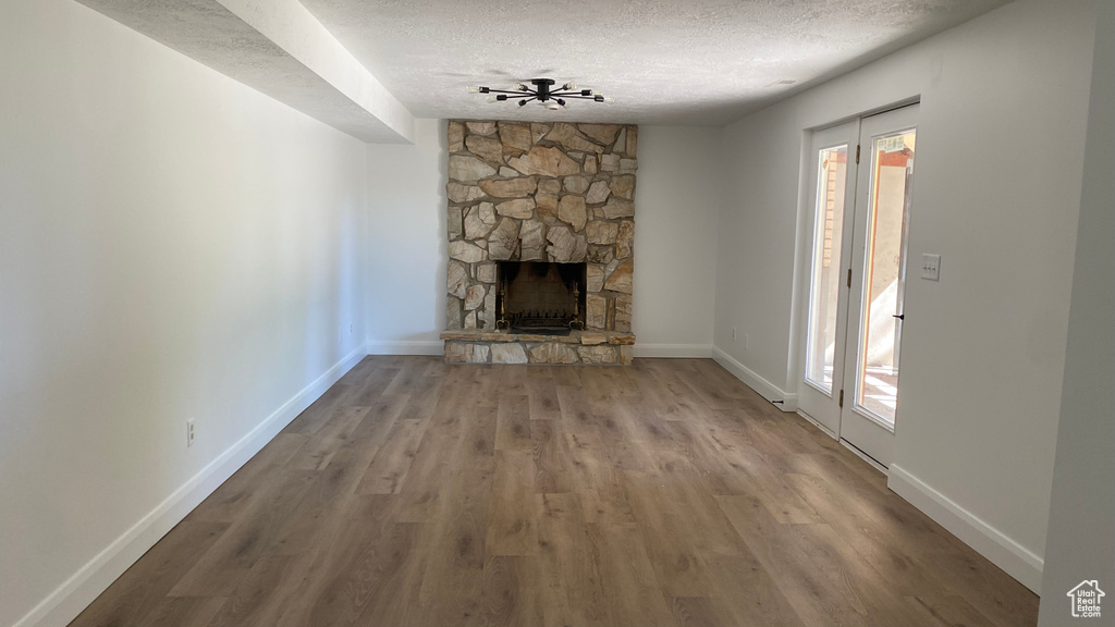 Unfurnished living room with hardwood / wood-style floors, a stone fireplace, a textured ceiling, and plenty of natural light